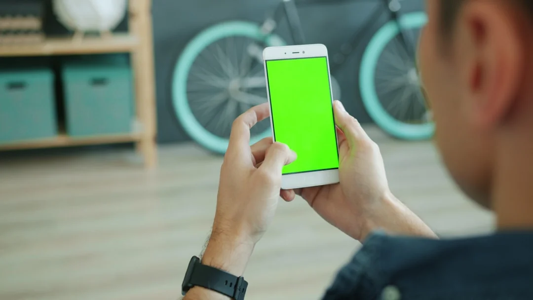 A person reviews stock market data on a smartphone and laptop while indoors.
